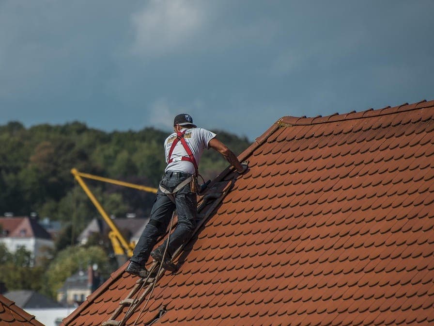 Handwerker mit Sicherungsgurt auf einer Leiter am Hausdach